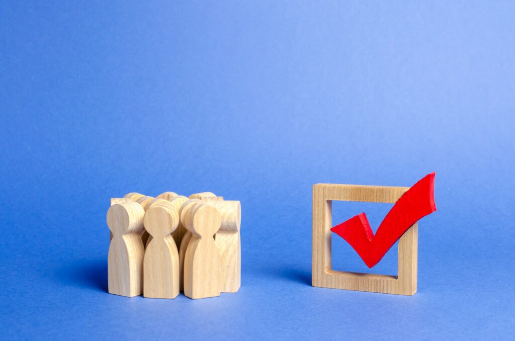 Crowd of people looking at a red wooden checkmark for voting on elections on a blue background