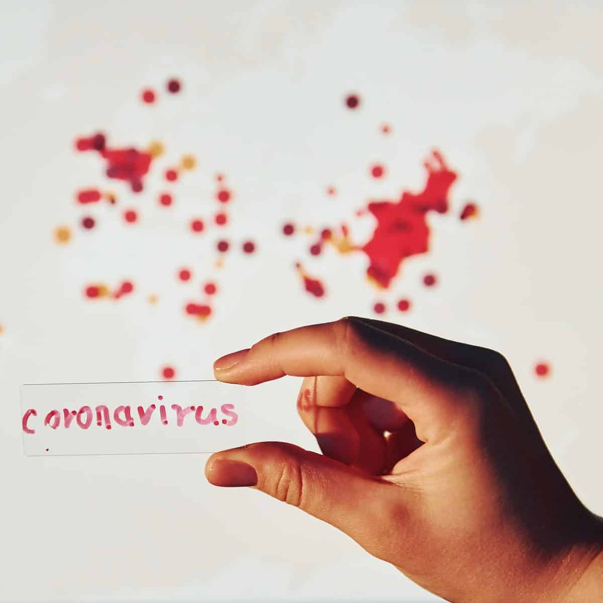 Man's hand holds lens with coronavirus title on it against background with world map of infection