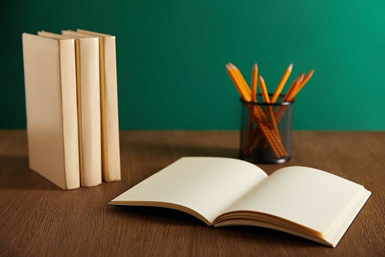open textbook, books and pencils on wooden table